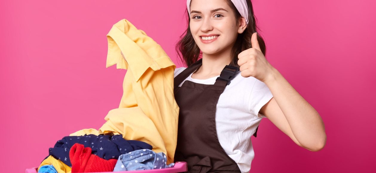 Portrait of energetic positive cute female looking directly at camera with happiness, standing isolated over bright pink background in studio, making sign super with her hand, looks delighted.